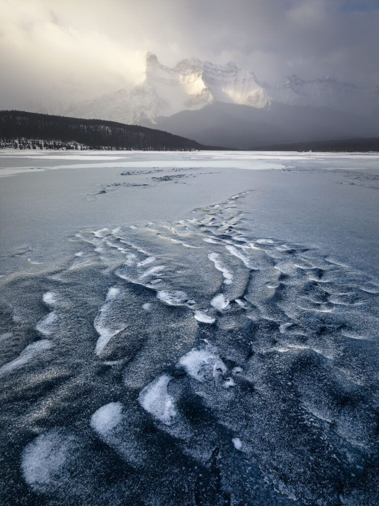 ripples in lake ice lead up to a snow storm mountain