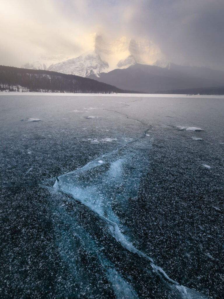 cracks in lake ice leading to dramatic mountain peak in snow storm