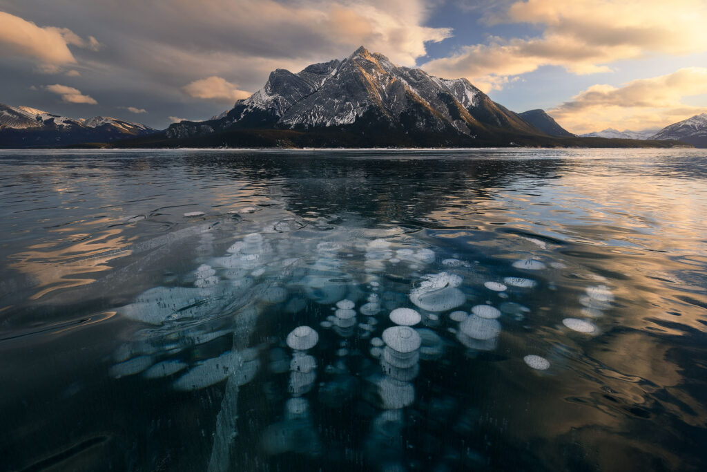 methane bubbles on a frozen lake under mountains at sunset
