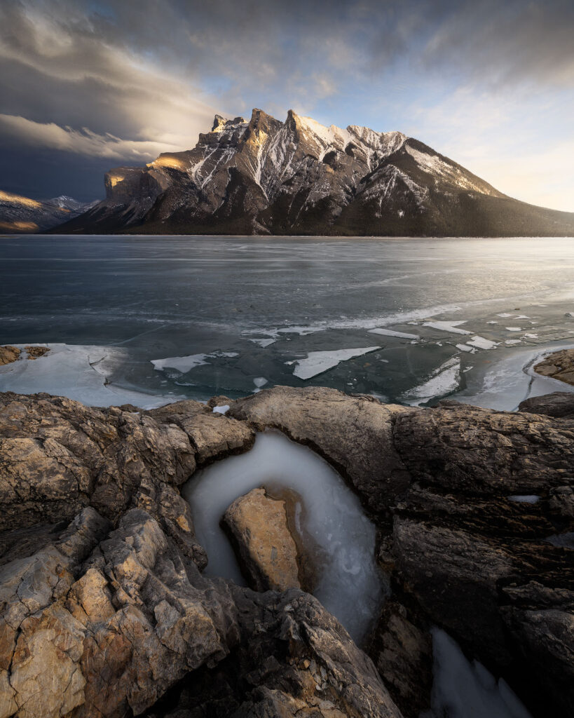 A Chinook looms over a large mountain and frozen lake at sunset