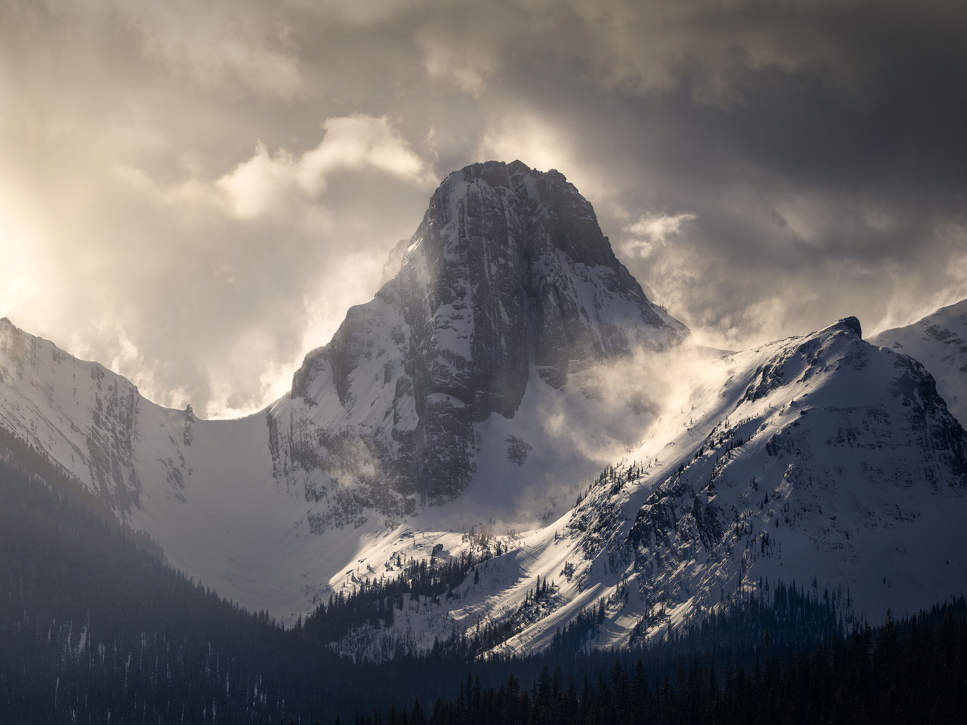 Taking flight-2026-P Back-lit snow blows off a dramatic mountain peak, creating an aura of glowing sky
