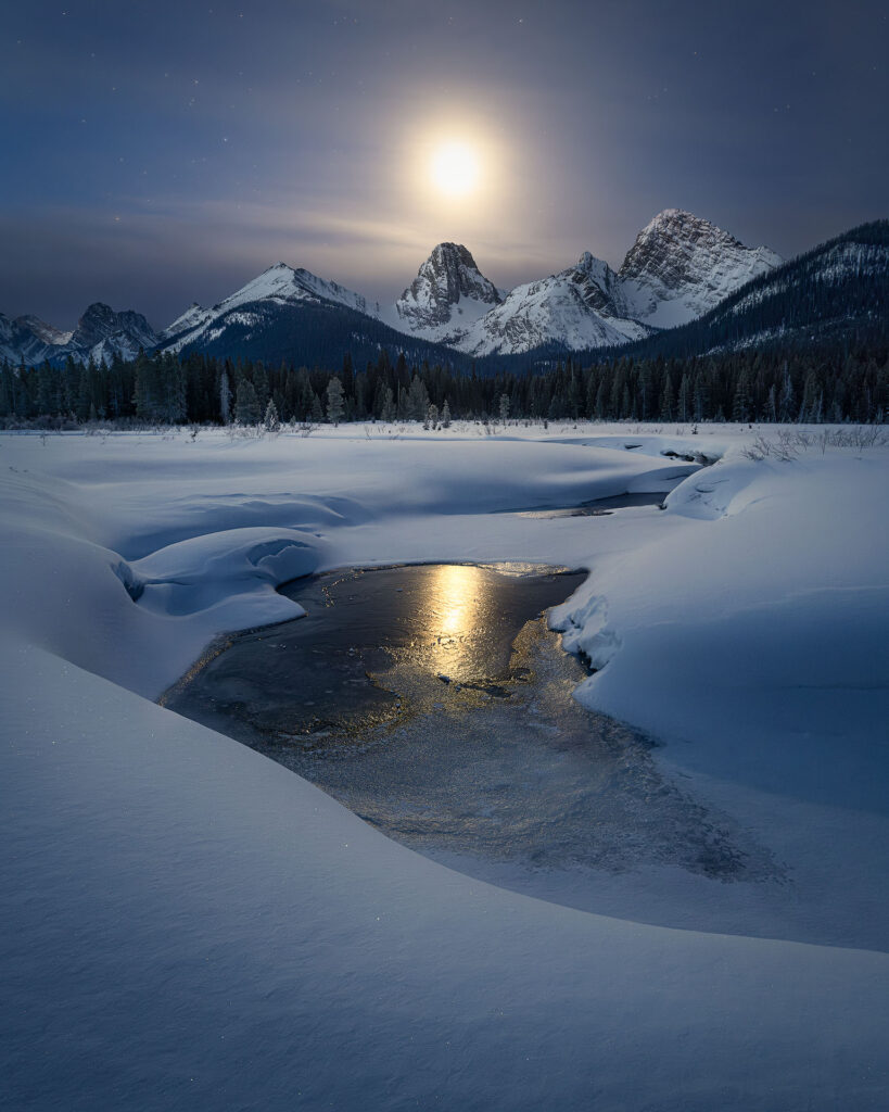 The moon sets over a winter mountain landscape
