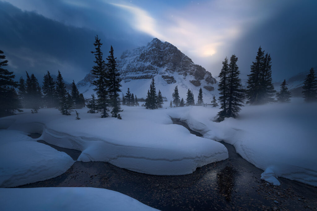The moon breaks through early morning clouds over Bow Lake